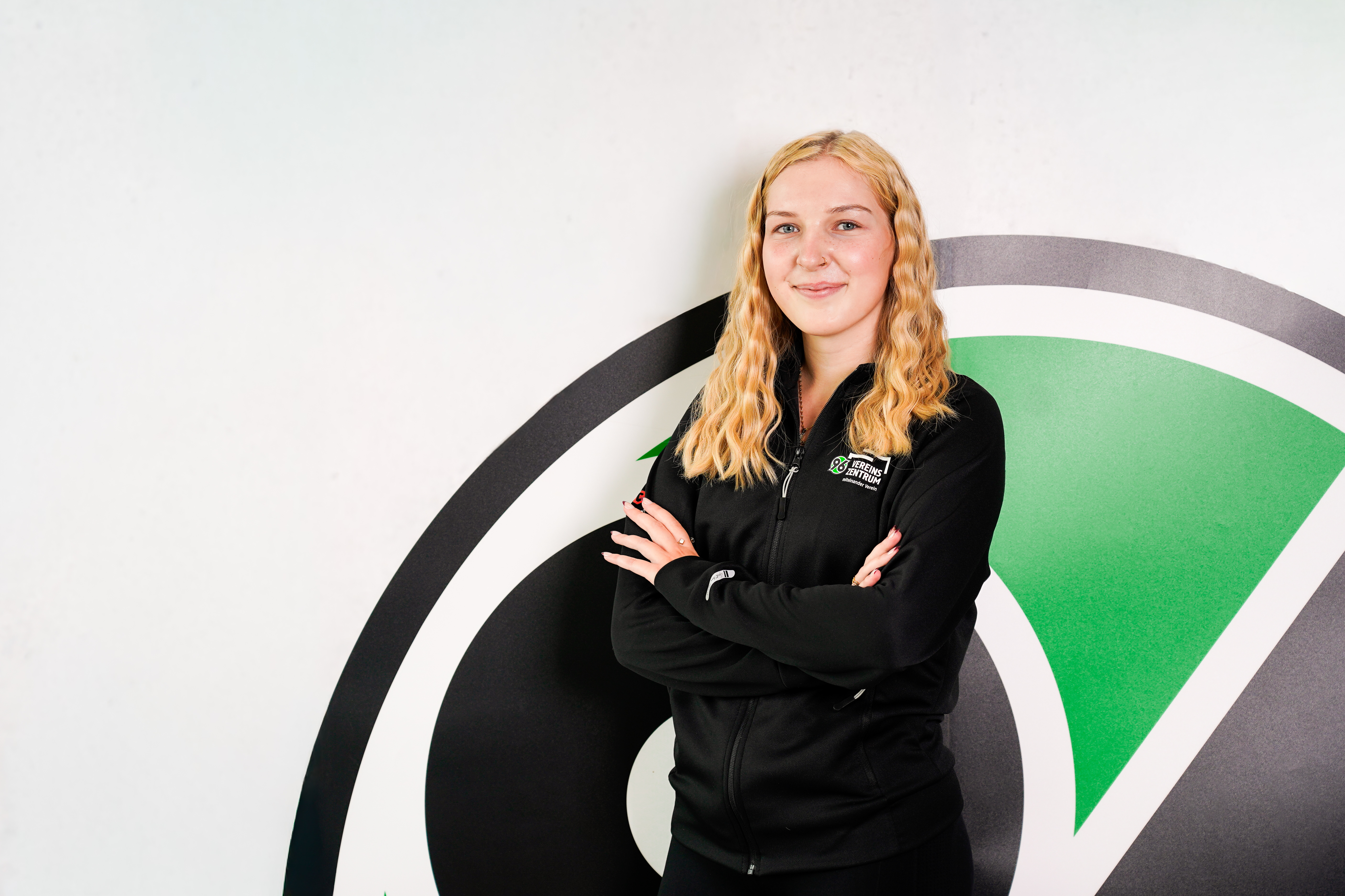Person lächelt mit verschrenkten Armen in die Kamera.