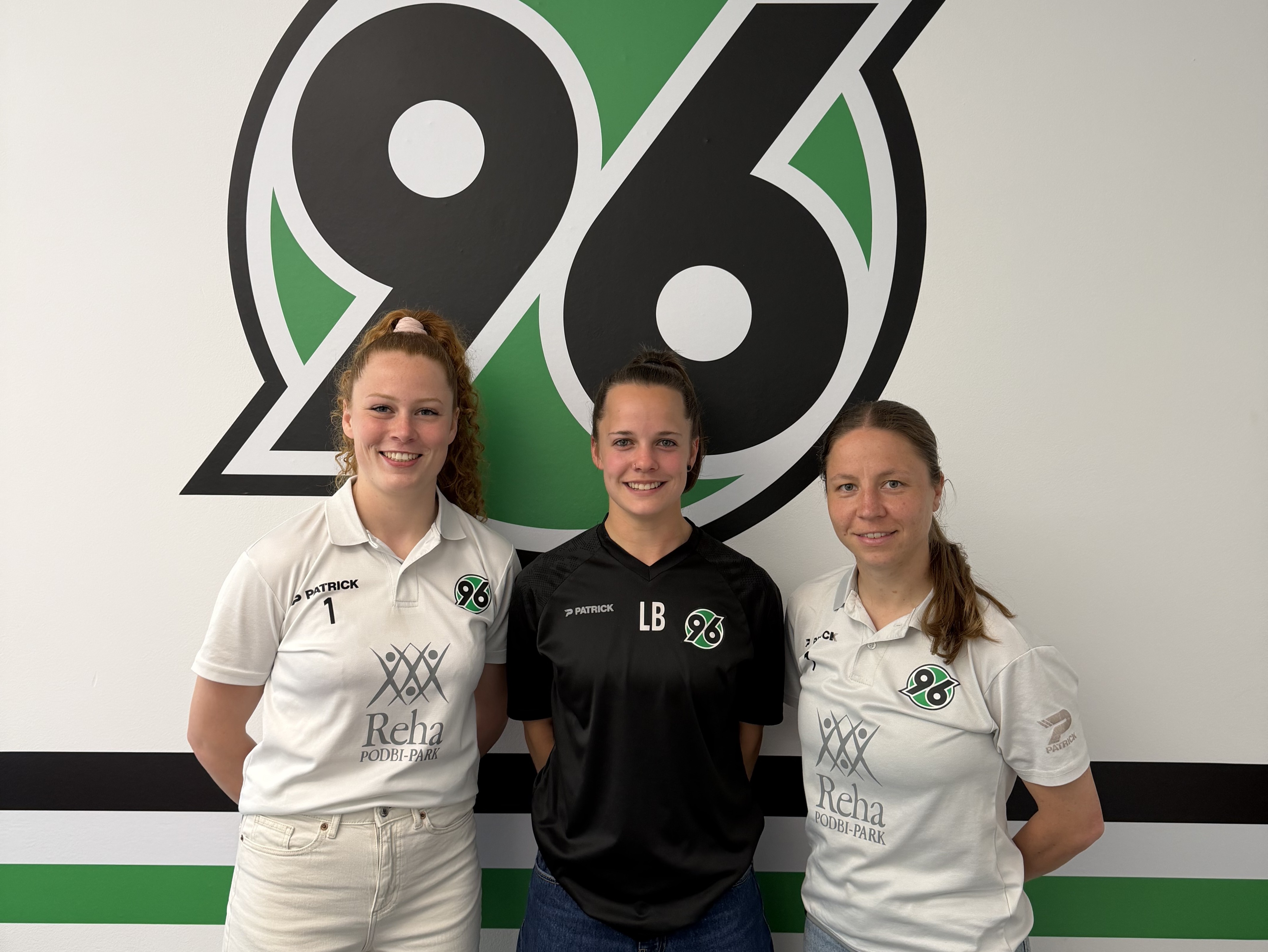 Drei Frauen stehen vor dem 96-Logo.