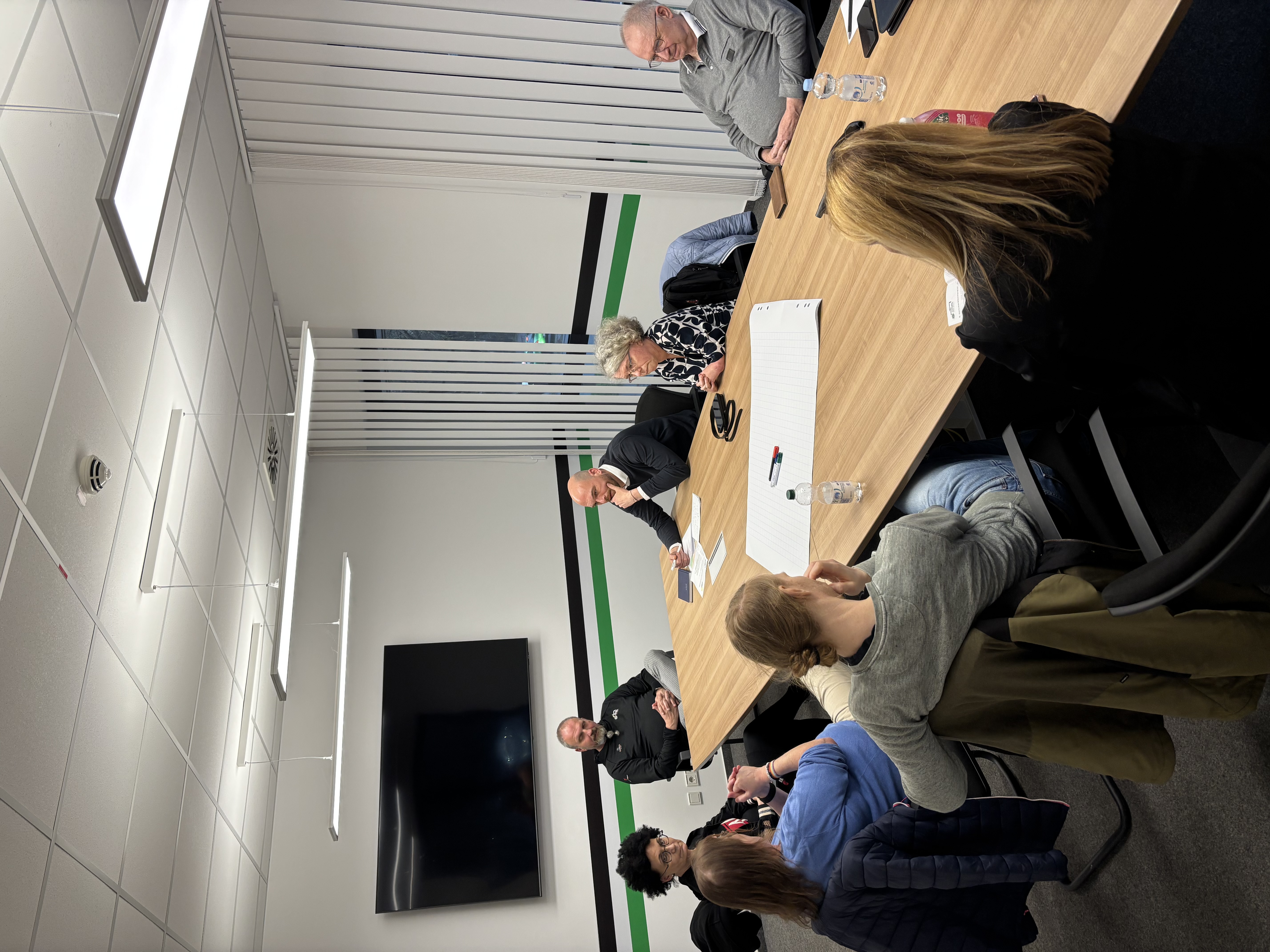 Acht Personen, darunter Holger Apitius (Inklusionsbeauftrager von Hannover 96) diskutieren an einem Tisch im Besprechungsraum des Vereinszentrums sitzend