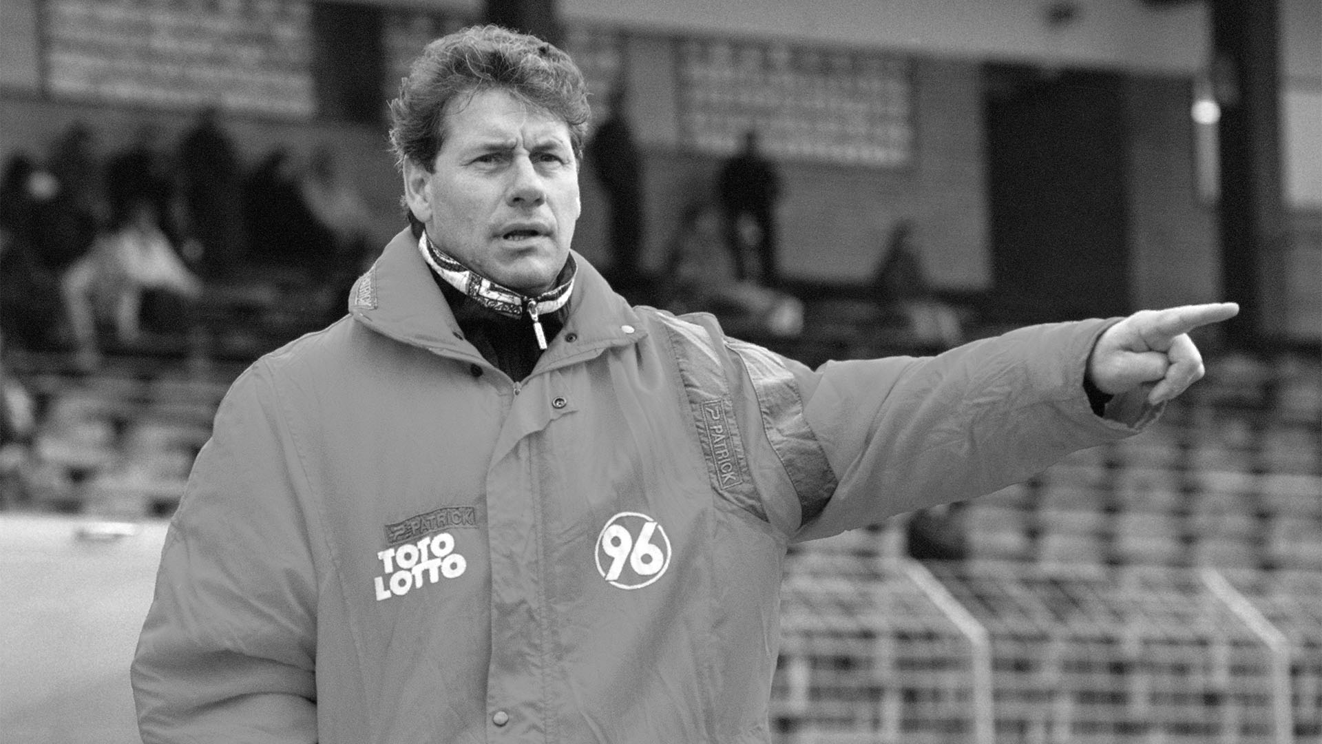 Schwarz-weiß-Foto des ehemaligen 96-Trainers Ebergard Vogel in einer weiten 96-Jacke, er zeigt nach links.