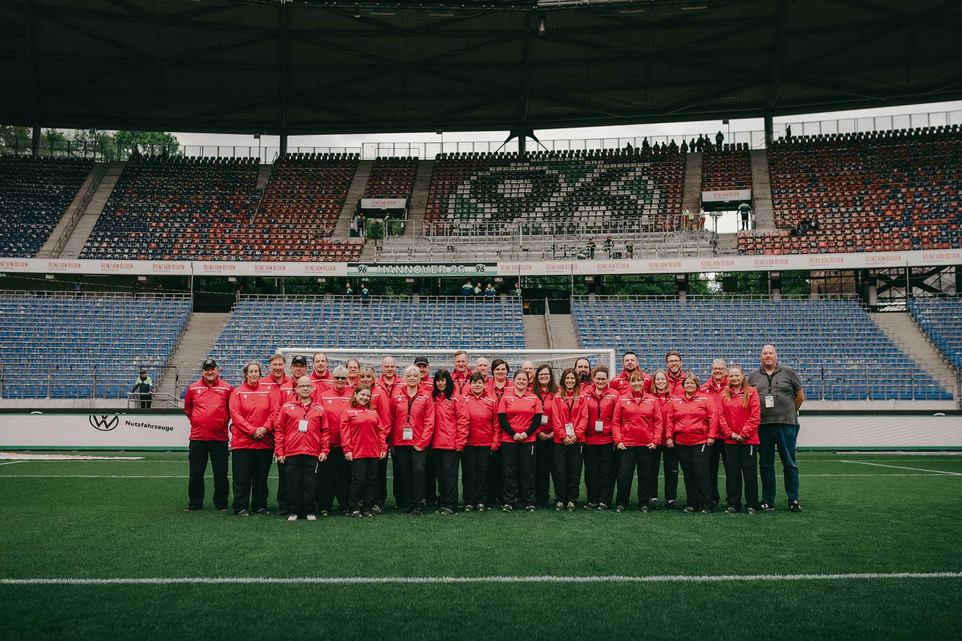 Das 96-Volunteers-Team - bestehend aus rund 30 Personen - steht in roten Jacken in der leeren Heinz von Heiden Arena. 