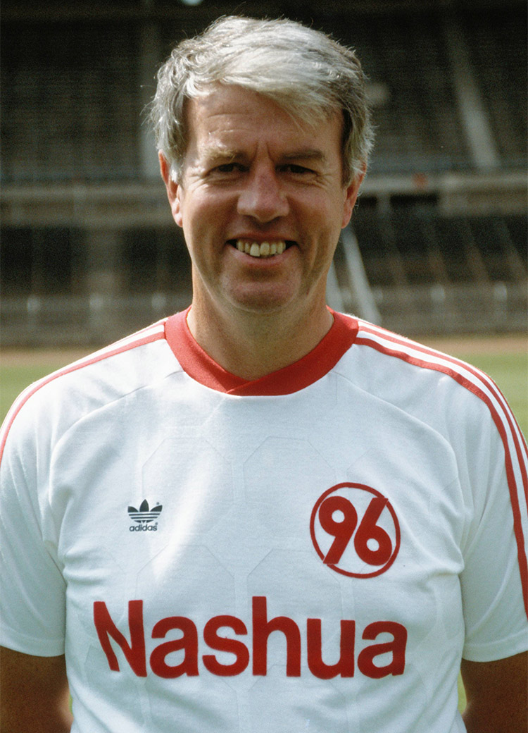 Jürgen Wähling lächelnd im weißen Adidas-Shirt mit einer roten 96 darauf.