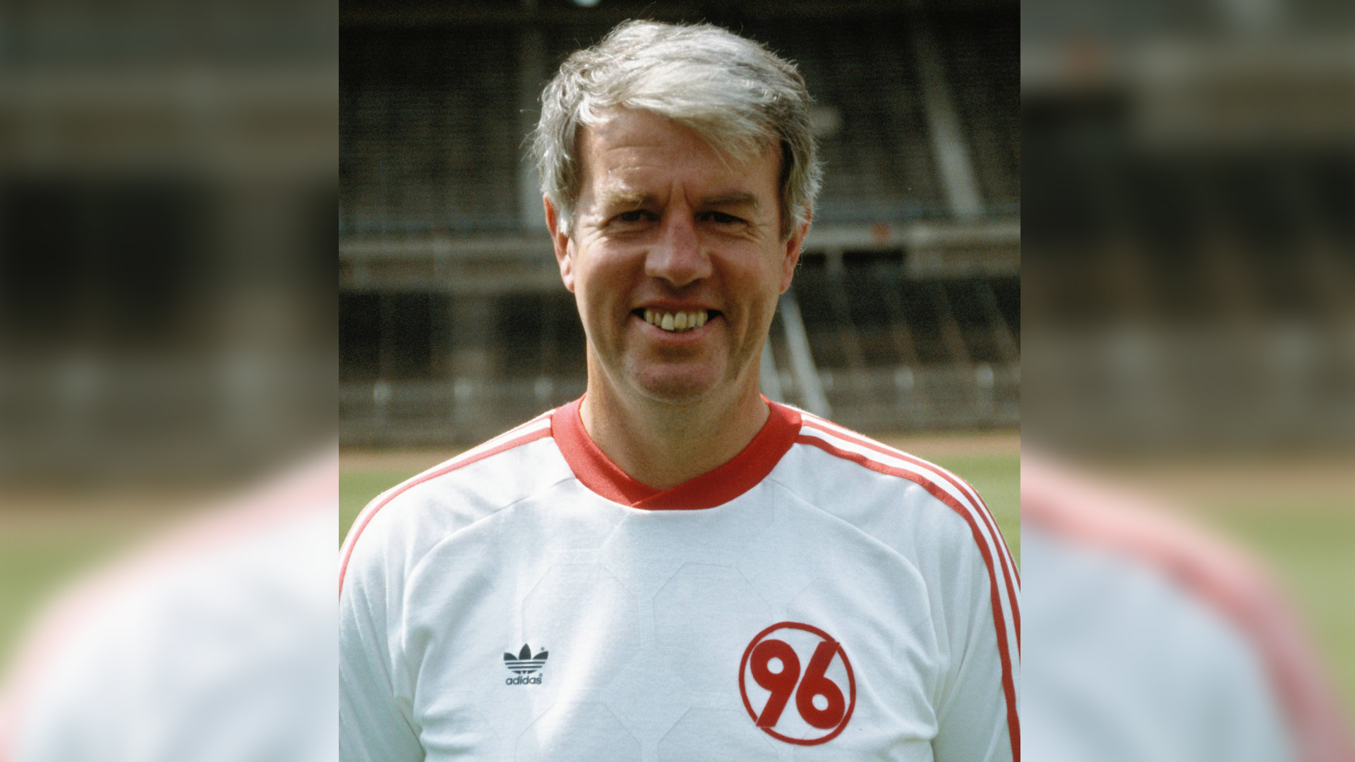 Jürgen Wähling lächelnd im weißen Adidas-Shirt mit einer roten 96 darauf.