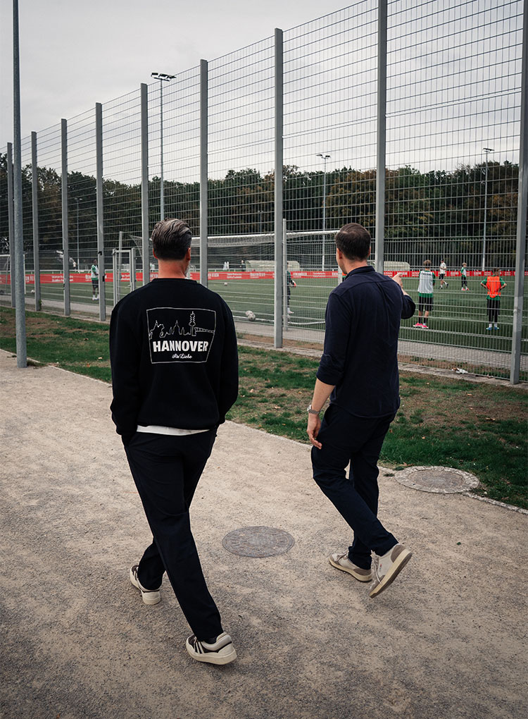 Sandro Wagner und Julian sind von Hinten beim Herumlaufen zu sehen, sie schauen auf einen Platz, auf dem eine Jugendmannschaft trainiert.
