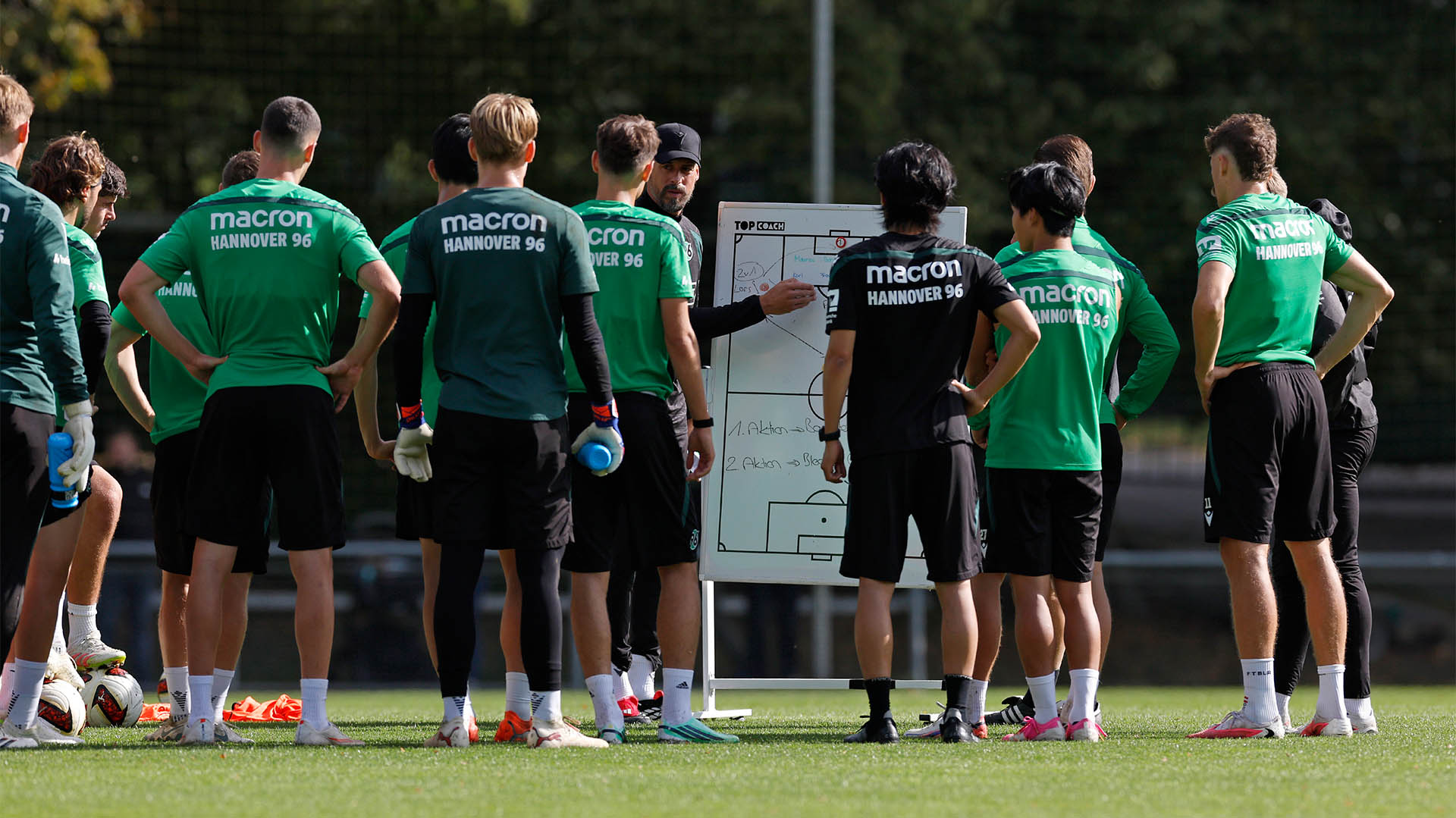 Der 96-Trainer Sandro Wagner steht vor einer Taktiktafle und erklärt einigen Spielern etwas auf dem Trainingsplatz.