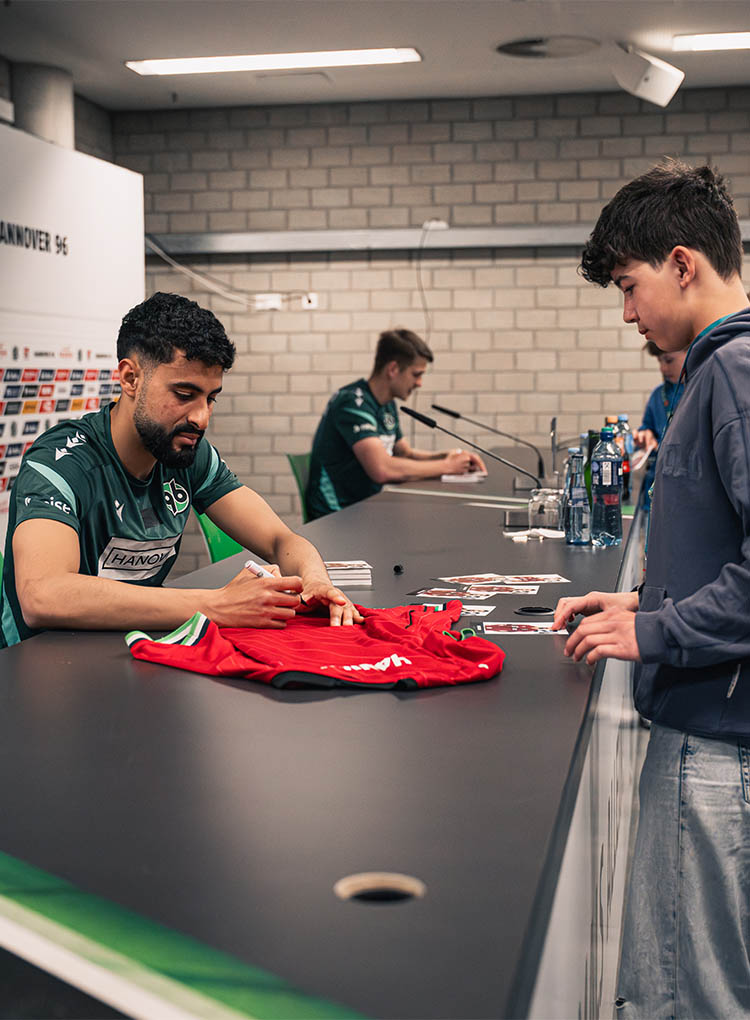 Elias Saad unterschreibt ein rotes 96-Trikot eines Jungen.