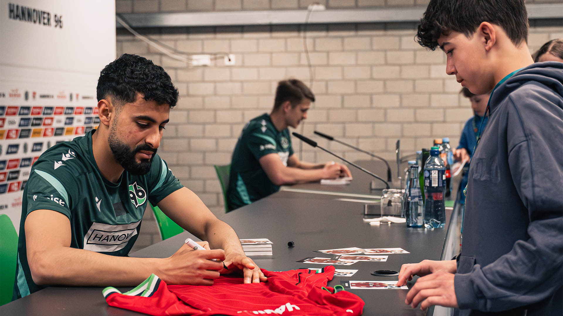 Elias Saad unterschreibt ein rotes 96-Trikot eines Jungen.