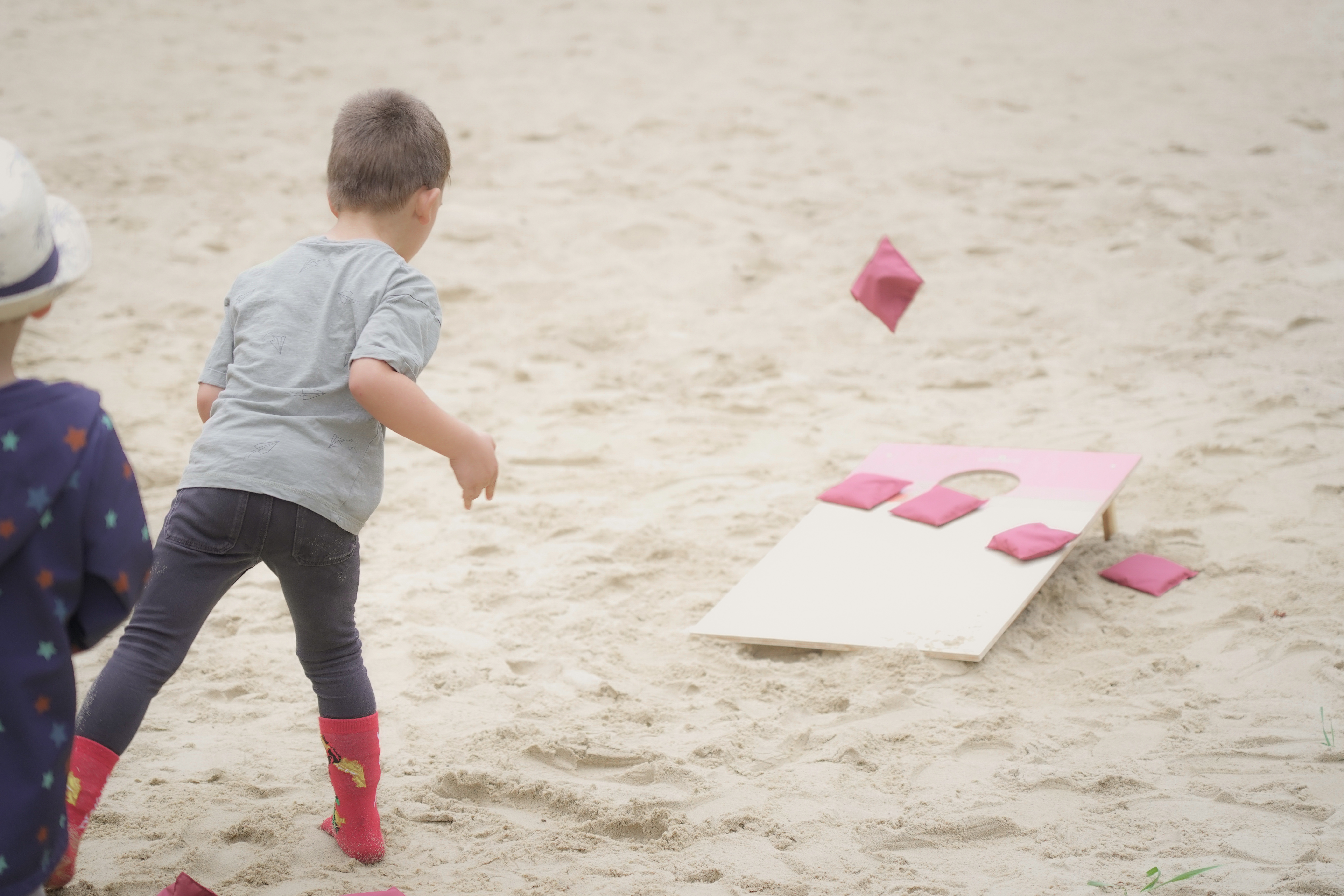 Kind wirf beim Zielwerfen einen Sandsack in das Loch.