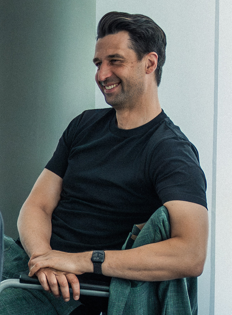 Jonas Boldt, sitzend in einem schwarzen Büro am Lachen.
