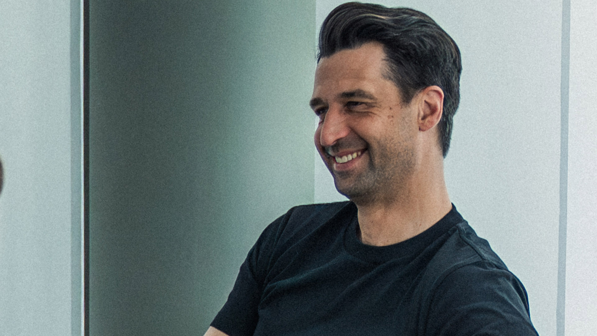 Jonas Boldt, sitzend in einem schwarzen Büro am Lachen.