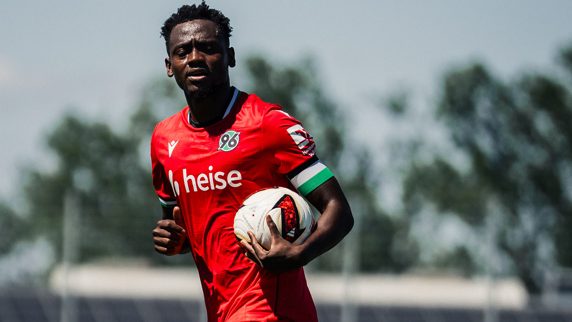 Mustapha Bundu trägt im roten 96-Trikot den Ball.