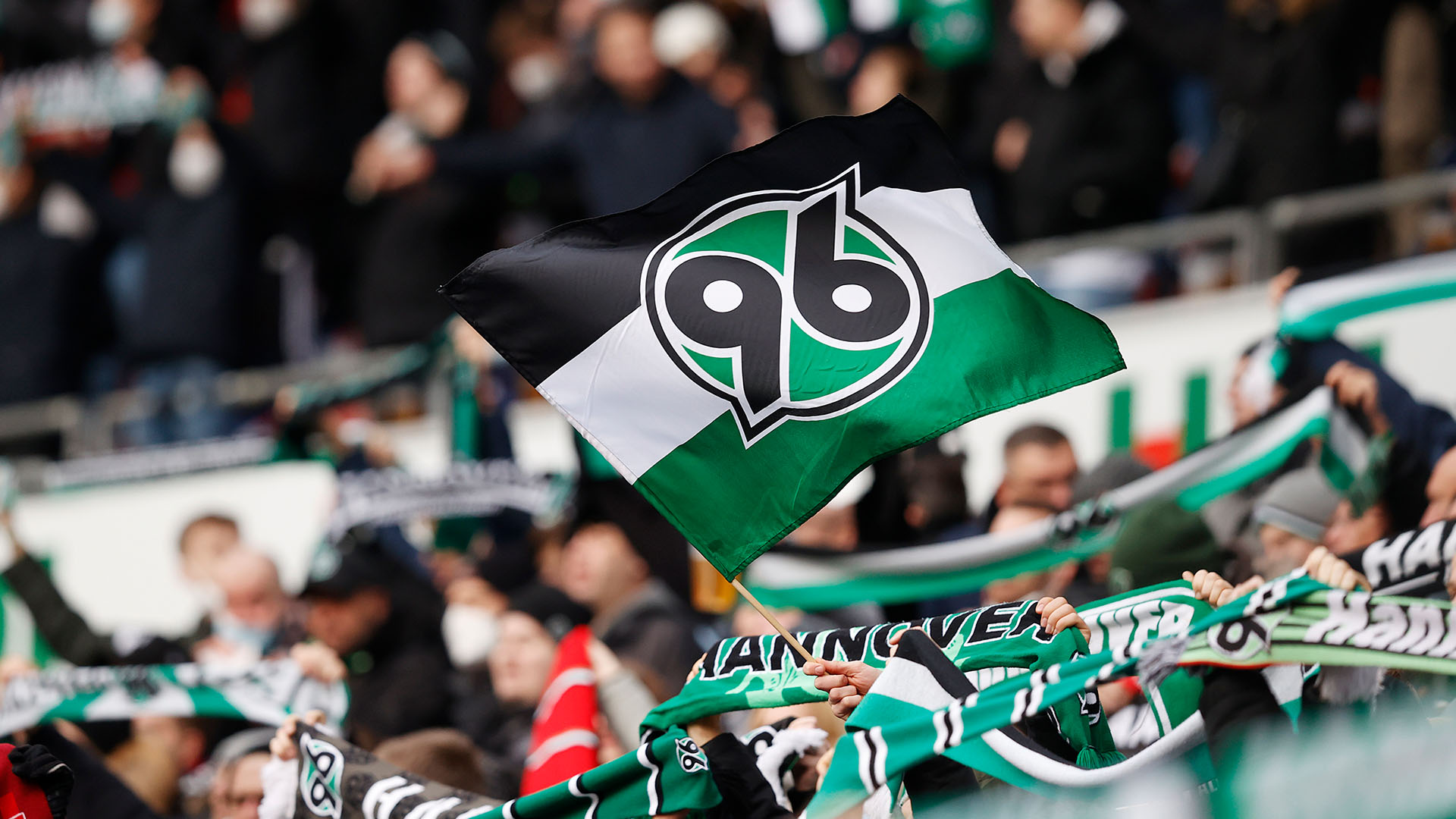 Hannover 96 Fans mit einer 96-Fahne im Vordergrund.
