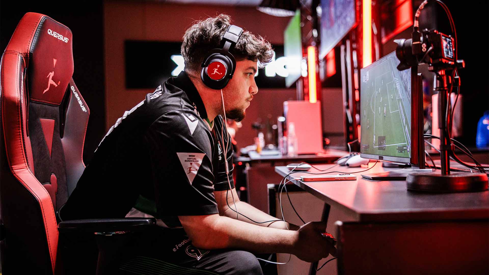96-eFootball-Profi seitlich aufgenommen, mit Kopfhörern, im Trikot und konzentriert an der Konsole.