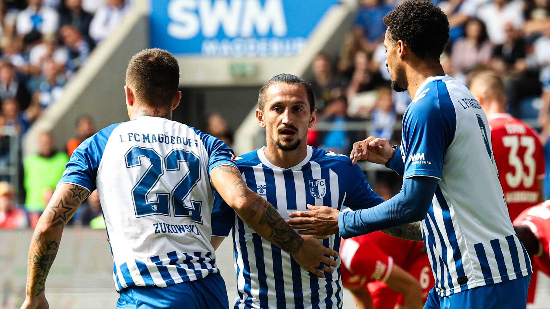 Drei Magdeburg-Spieler in blau-weißen Trikots klatschen ab.