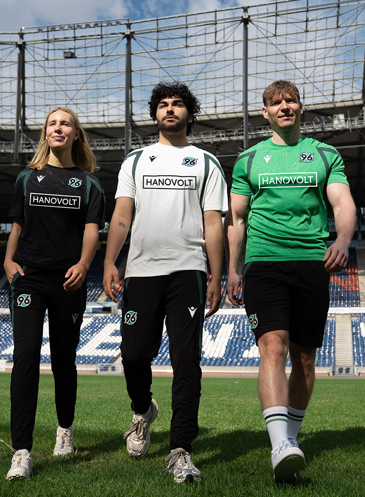 Eine Frau und zwei Männer in schwarzer, weißer und grüner Trainingskleidung im Stadion.