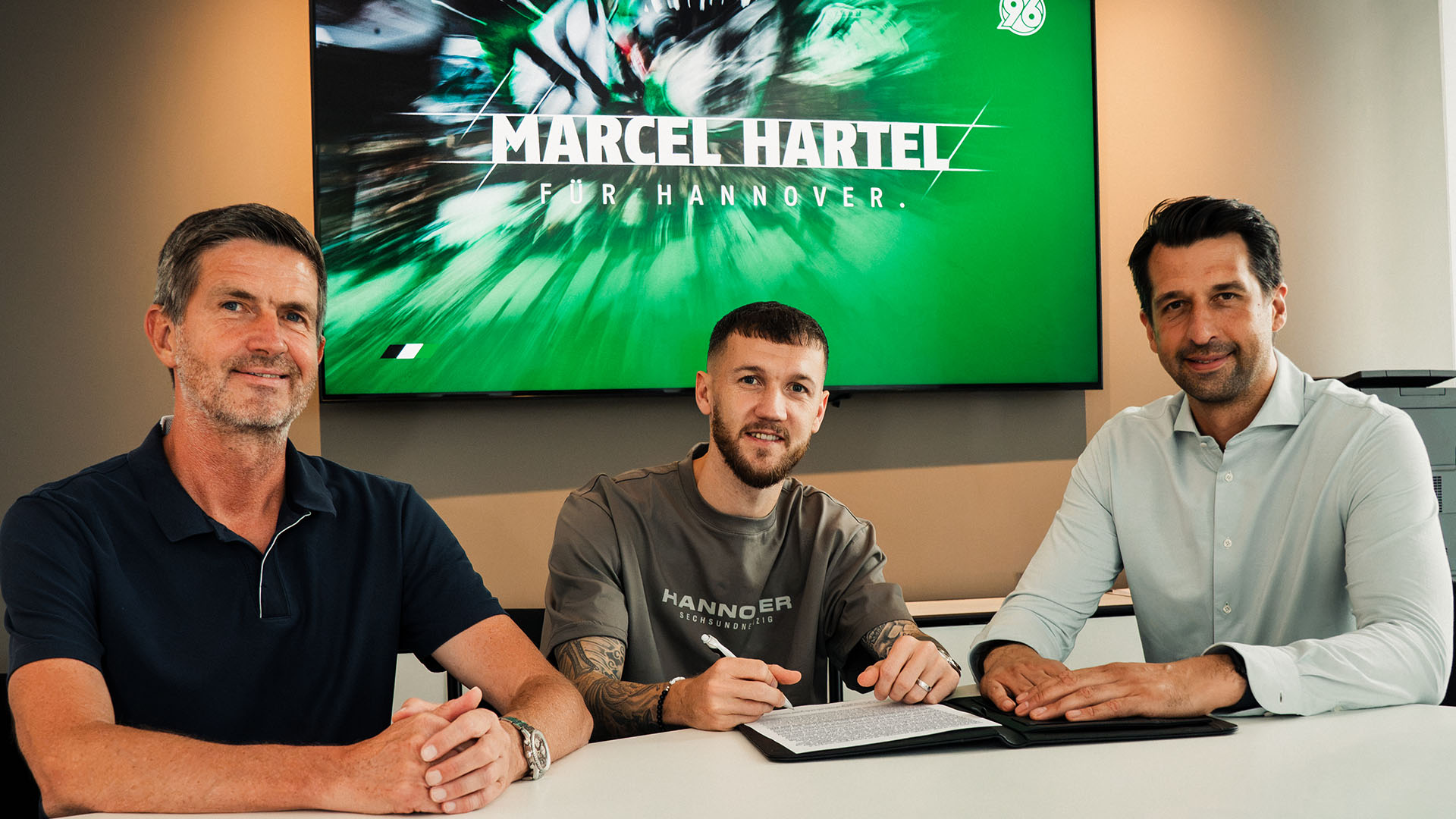 Marcel Hartel unterschreibt seinen Vertrag, flankiert von Ralf Becker (links) und Jonas Boldt (rechts).