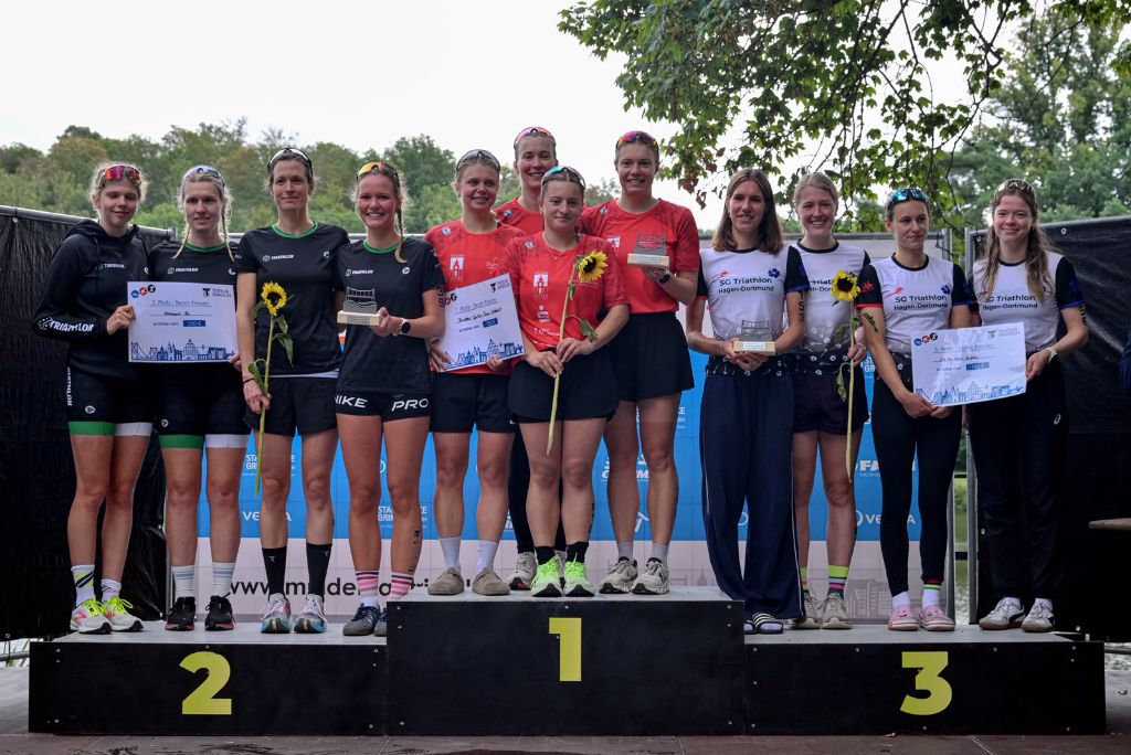 Drei Teams stehen mit Urkunden auf einem Podest.