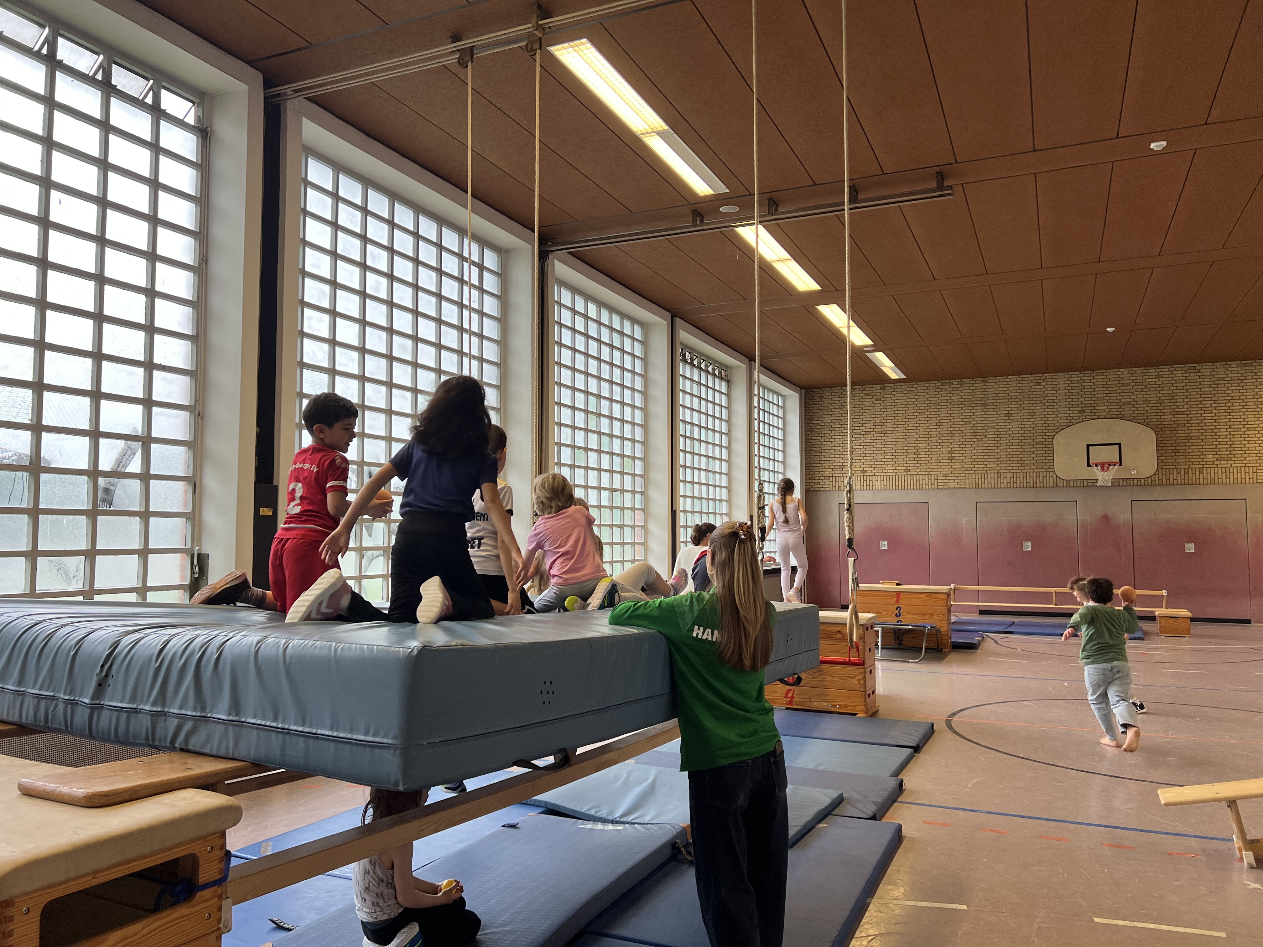 Kinder turnen unter Aufsicht der Übungsleiterin auf einer Matte