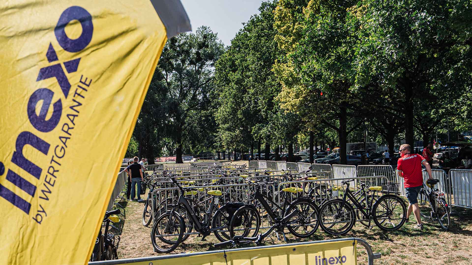 Blick auf einen Fahrradstellplatz auf einer Wiese, im Vordergrund steht eine gelbe linexo-Beachflag.