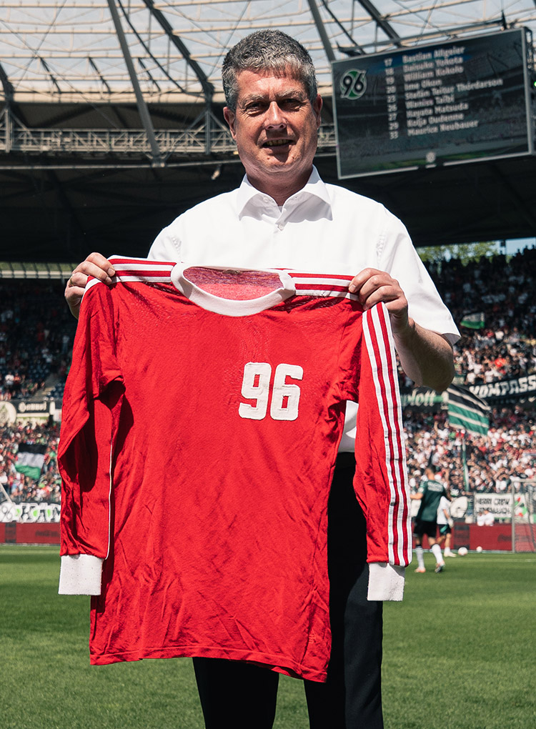 Ein Mann hält im Stadion ein historisches 96-Trikot in die Kamera.
