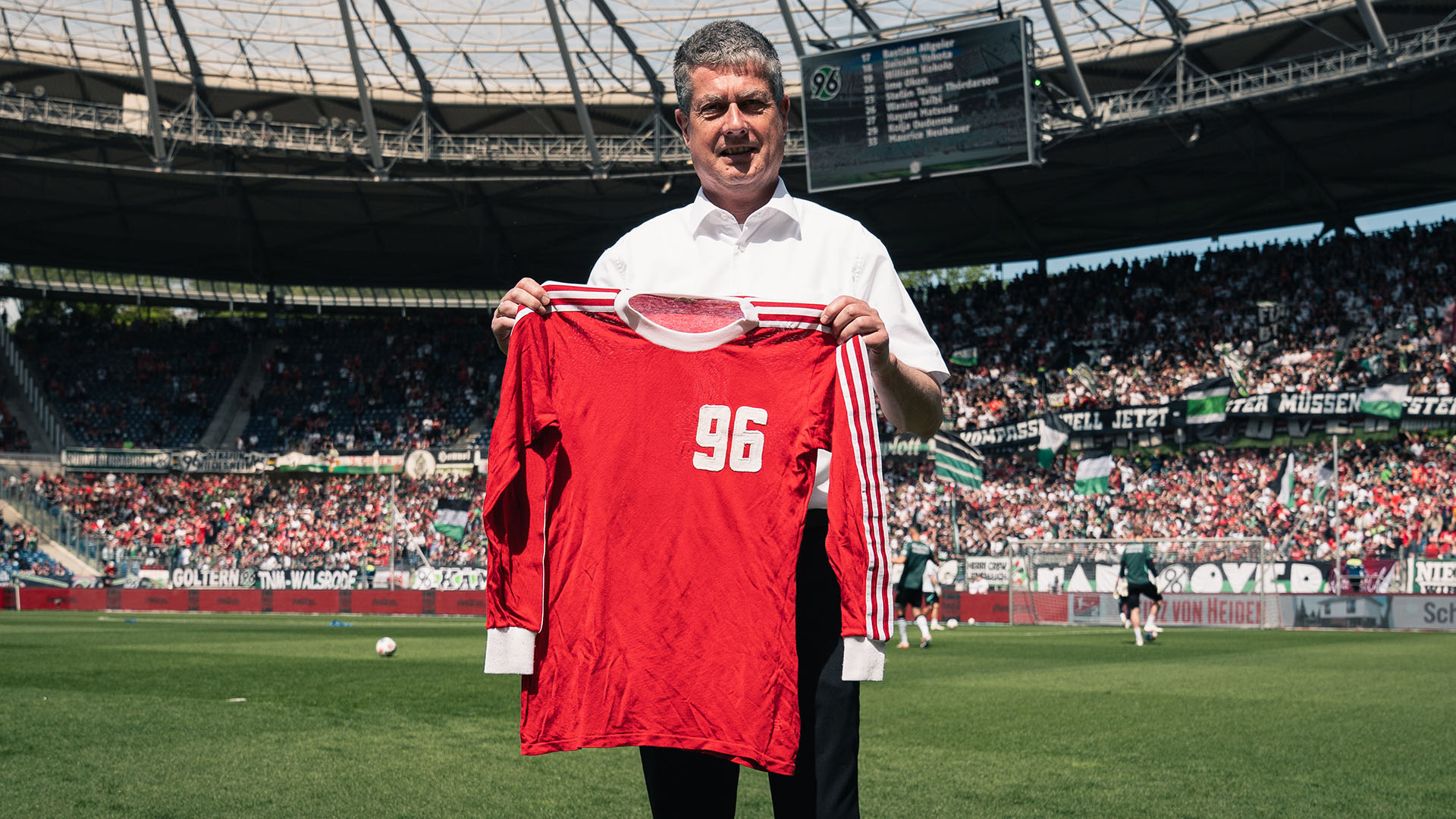 Ein Mann hält im Stadion ein historisches 96-Trikot in die Kamera.