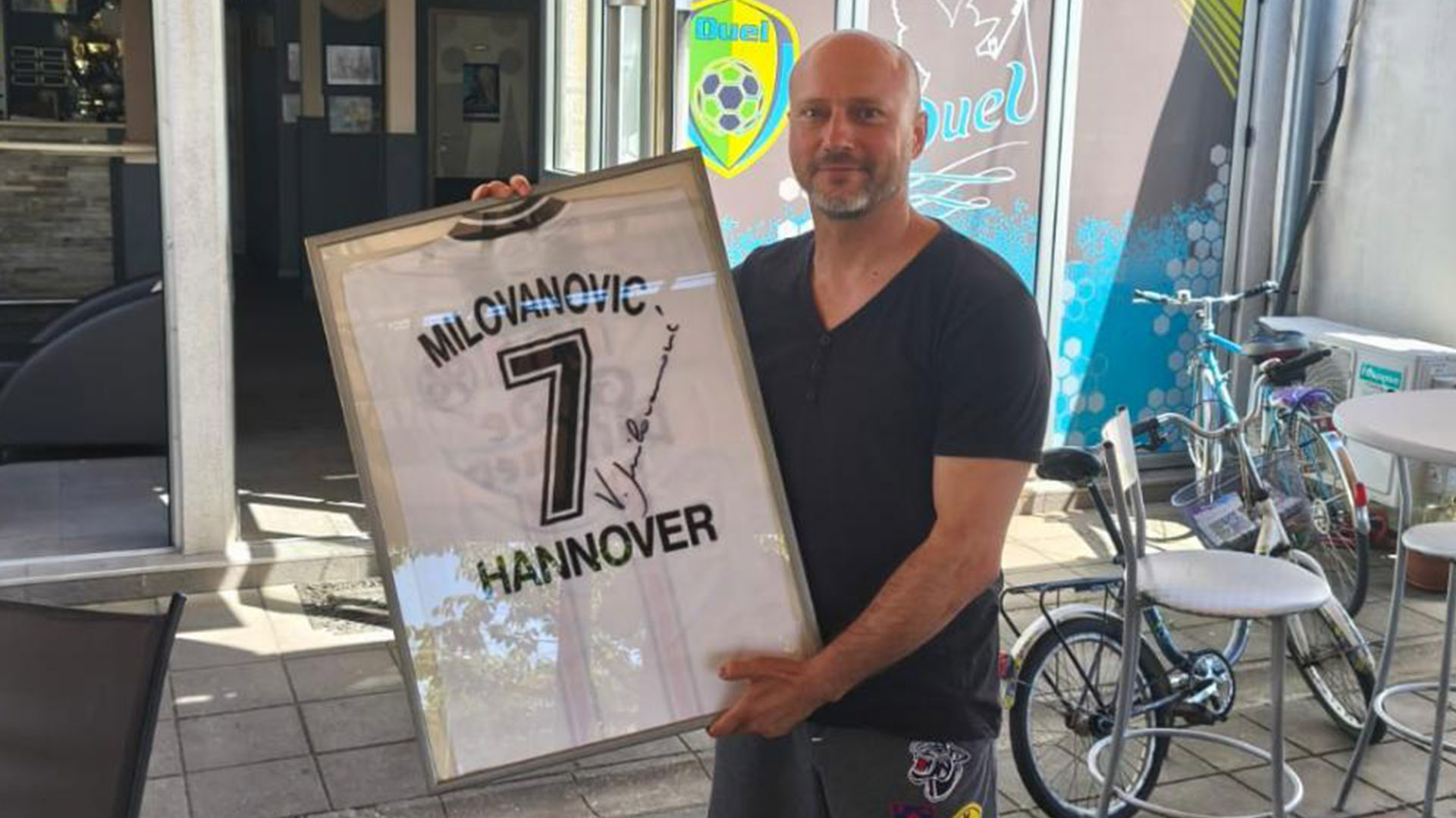 Vladan Milovanovic hält das gerahmte Trikot in die Kamera.