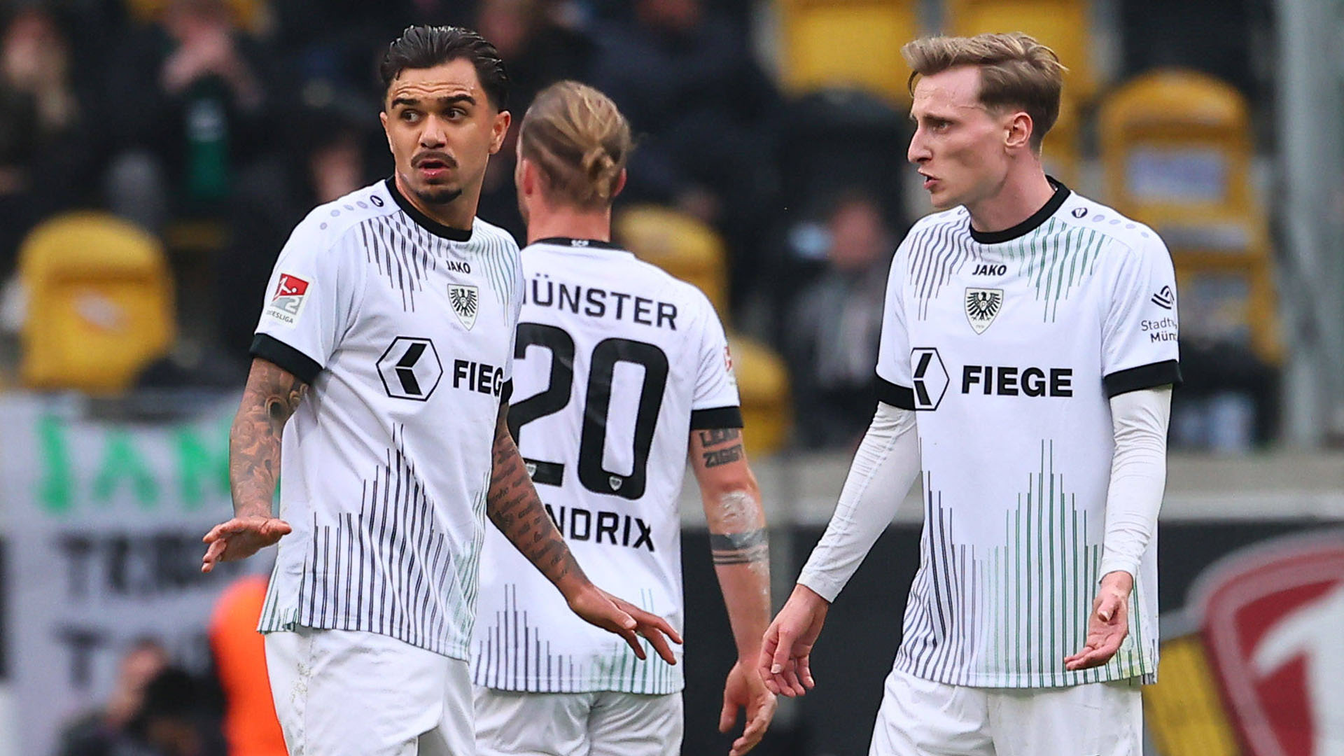 Drei Münster Spieler in weißen Trikots.