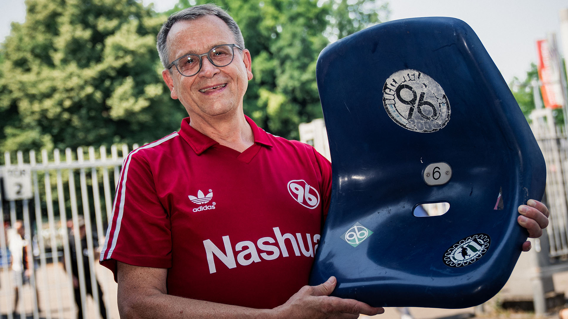 Ein Mann hält im roten 96-Trikot eine blaue Sitzschale.