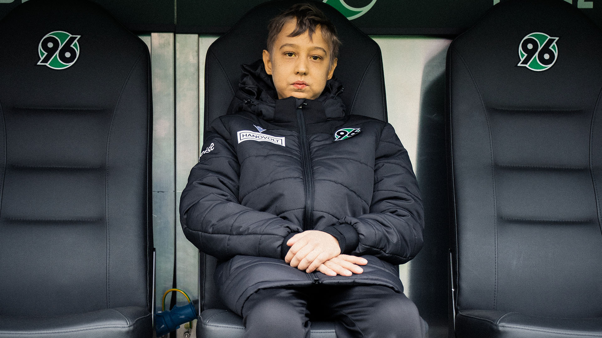 Vladislav sitzt in schwarzer Jacke auf der Auswechselbank.