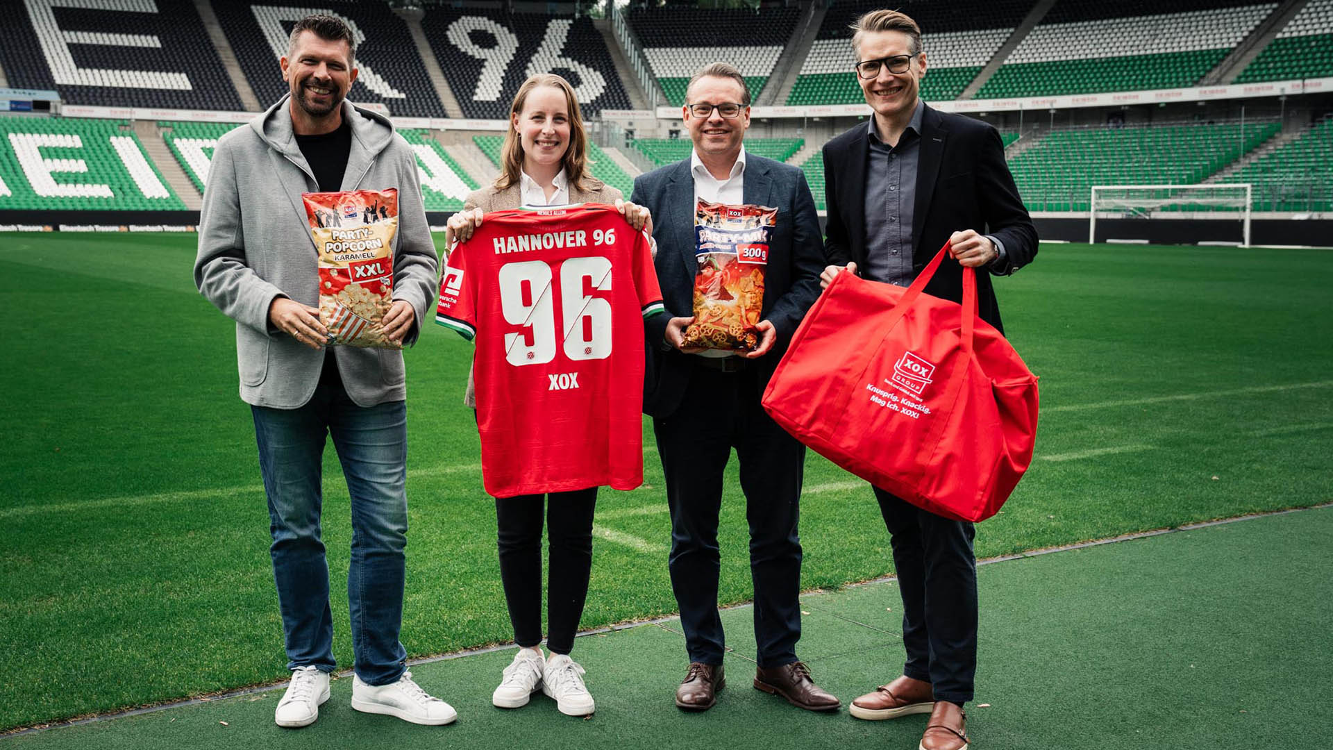 Vier Personen im Stadion halten XOX-Produkte und ein beflocktes 96-Trikot mit XOX hoch.